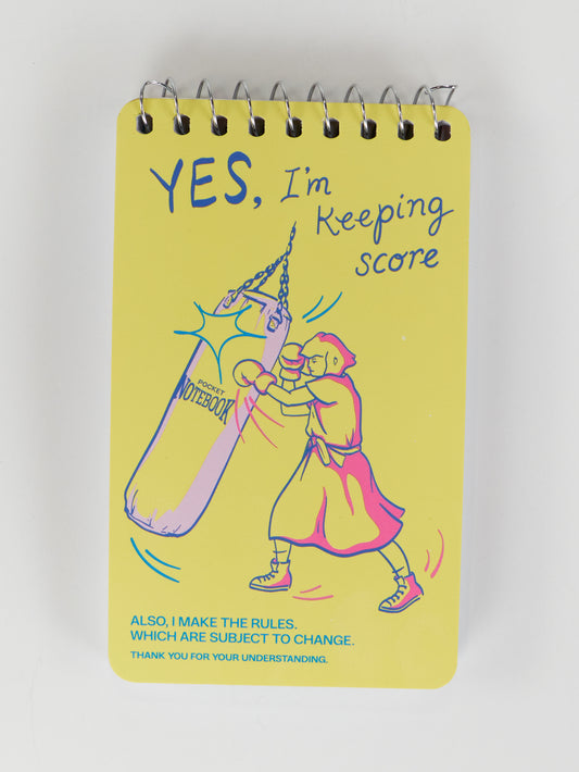 The Blue Q "Yes, I'm Keeping Score. Also, I Make The Rules Which Are Subject To Change. Without Notice." 3x5 spiral notebook features a yellow cover with a gym-inspired illustration and witty text.