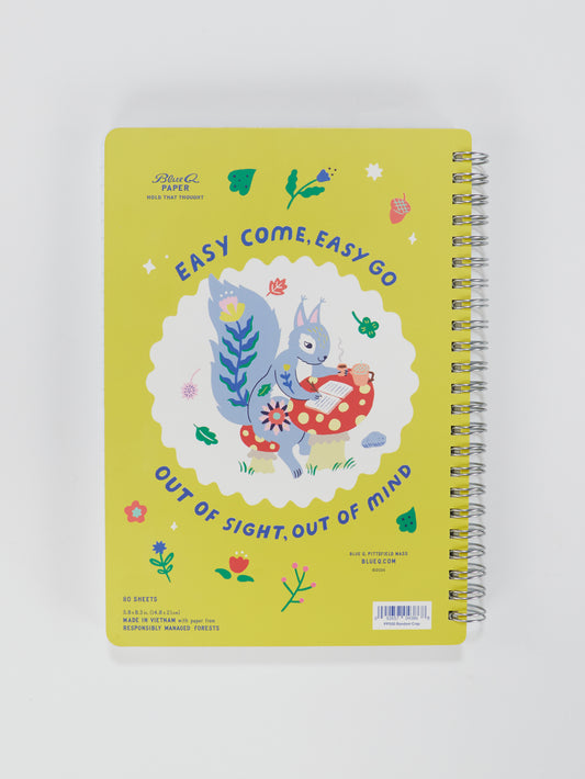 The Blue Q Random Crap 6x8 Spiral Notebook features a yellow cover with a gray squirrel holding a cup on a red mushroom, surrounded by flowers and leaves. Text reads: EASY COME, EASY GO, OUT OF SIGHT, OUT OF MIND.