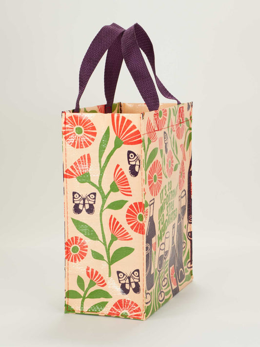 The Blue Q "It's So Important To Stay Hydrated Handy Tote" is a reusable beige bag with purple handles, red flowers, green leaves, black butterflies, and bottles on the side panel reminding you that hydration is essential.