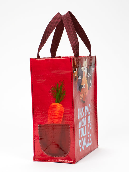 The Blue Q “This Bag Might Be Full Of Ponies Handy Tote” is a red eco-friendly bag with maroon handles, featuring a carrot, ponies, and whimsical text—ideal as a small everyday pony bag.