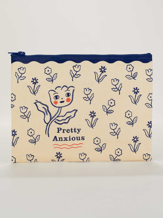 The Pretty Anxious Zipper Pouch by Blue Q is a beige pouch with a blue zipper, featuring blue and red floral art. The main flower has a face, with "Pretty Anxious" below—blending charm and nerves in one unique design.
