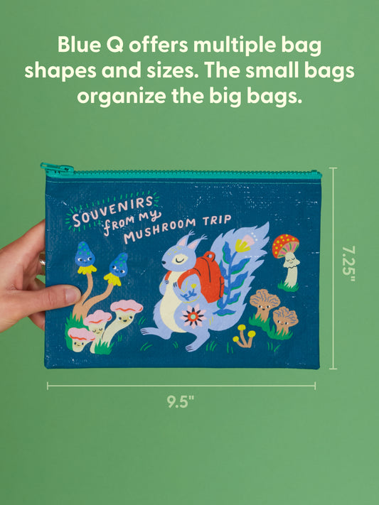 A hand holds Blue Q’s "Souvenirs From My Mushroom Trip" zipper pouch (9.5" x 7.25"), made from recycled material and featuring a squirrel with a backpack among colorful mushrooms—a fun, eco-friendly way to stay organized.