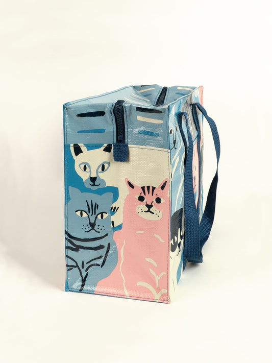 The Blue Q Happy Cats Shoulder Tote is a reusable rectangular bag with blue handles, featuring illustrated blue, pink, and white cats on its sides against a light background.