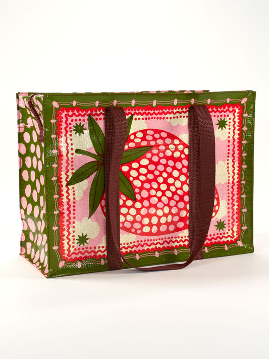 The Blue Q Strawberry Clouds Shoulder Tote features maroon handles, a bold red strawberry with white dots and green leaves on a pink and green background, plus pink polka dot sides—perfect for carrying strawberries or cream.