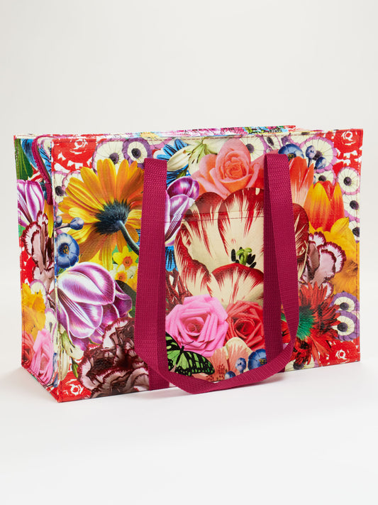The Blue Q Blossom Shoulder Tote is a reusable white bag with vibrant floral patterns in red, yellow, pink, and purple, and features dark pink handles.