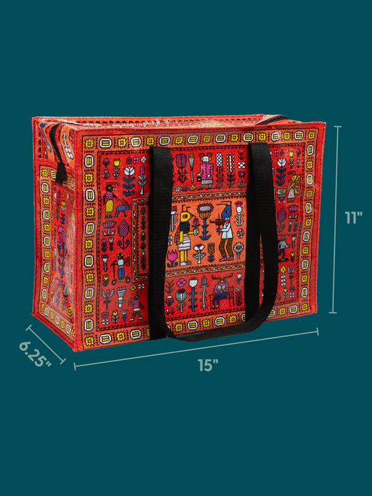 The Blue Q Magic Carpet Shoulder Tote is a colorful rectangular bag with black handles, featuring a vibrant folk-art pattern and a secure zipper closure. This sturdy tote measures 15″ wide, 11″ tall, and 6.25″ deep, and is displayed against a teal background.