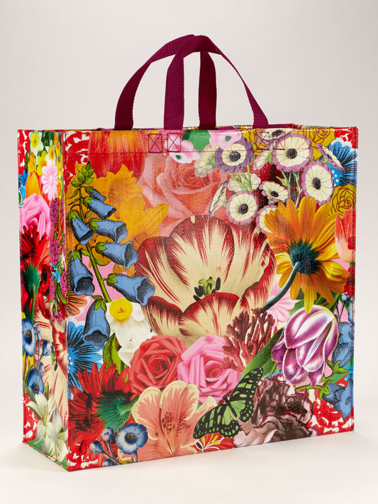 The Blossom Shopper by Blue Q is a large reusable bag with maroon handles, featuring a vibrant POWER flowers design—various flowers and a green butterfly on a crisp white background.
