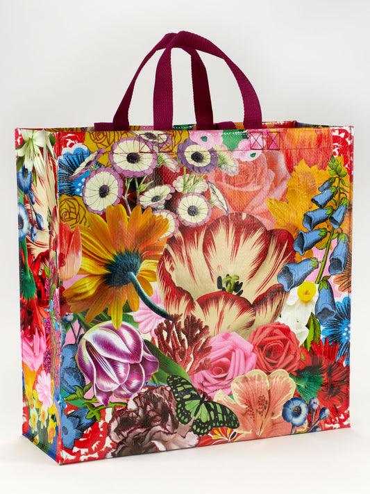 The Blossom Shopper by Blue Q is a reusable shopping bag with maroon handles, featuring a vibrant power flower and green leaf pattern on a white background.