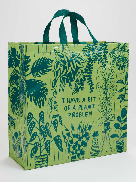 The Blue Q “I Have A Bit Of A Plant Problem Shopper” is a reusable bag with green handles, playful plant illustrations, and the phrase “I HAVE A BIT OF A PLANT PROBLEM” in the center.