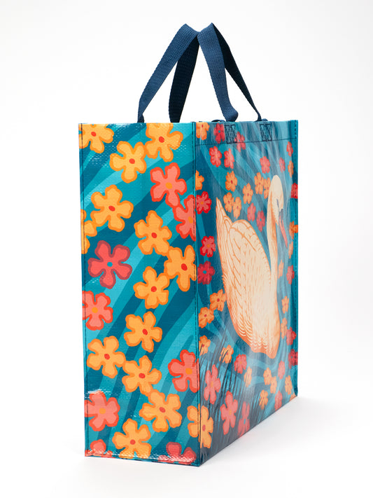 The Swan Shopper by Blue Q is a reusable, eco-friendly bag with navy handles, adorned with orange and pink flowers on a teal background and featuring a charming swan design.