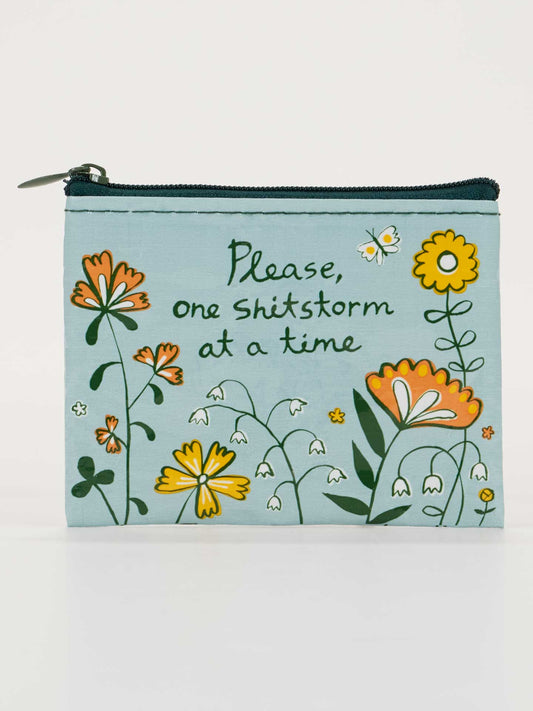 The Blue Q "Please, One Shitstorm At A Time" Coin Purse is a light blue zippered pouch made from recycled material, decorated with yellow, orange, and white flowers.