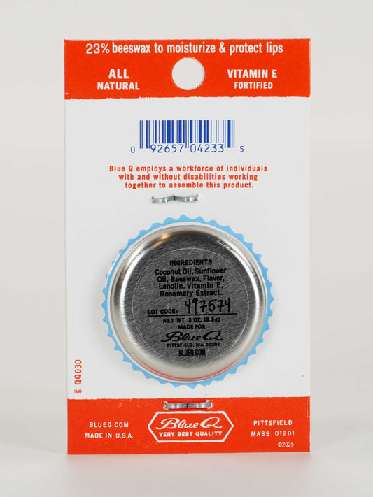 A tin of Blue Q Lip Shit Lip Balm-Sunny Clementine is attached to branded packaging. The card highlights 23% beeswax, Vitamin E, the ingredient list on the lid, and support for employment of people with disabilities.