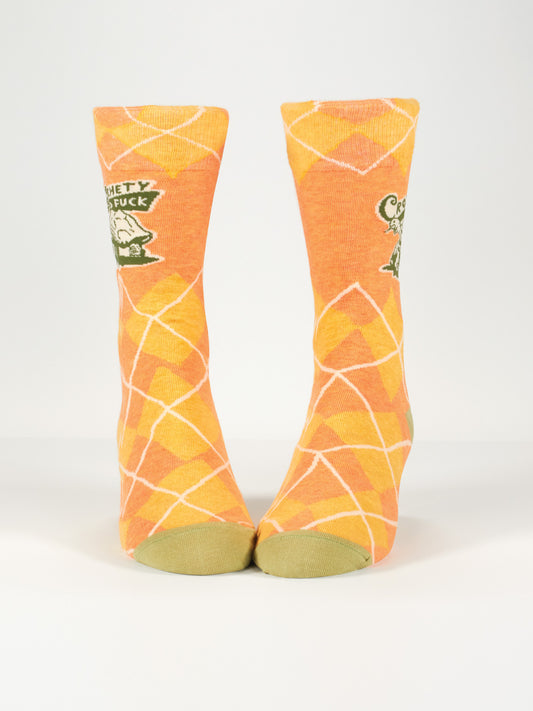 Blue Q’s Crotchety Old Fuck M-Crew Socks feature an orange and yellow argyle pattern, green toes, a cartoon design, and the phrase "Comfy as fuck" on the front of each sock.