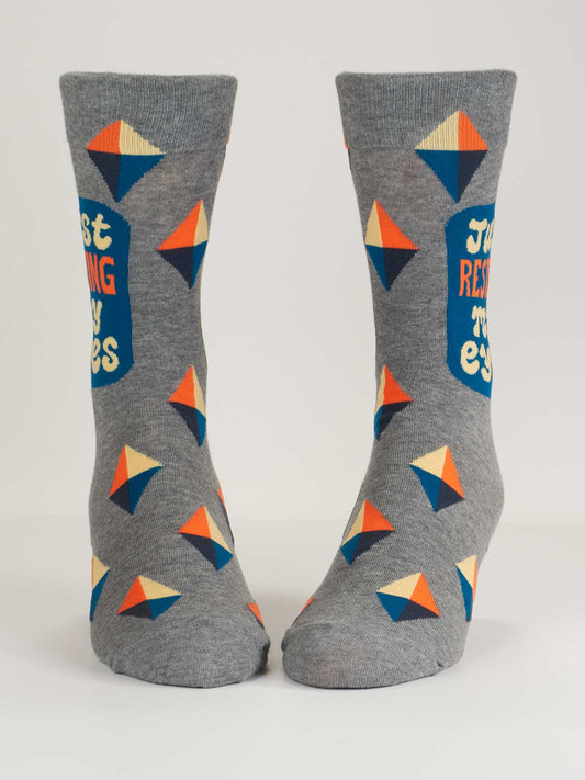 Blue Q’s Just Resting My Eyes M-Crew Socks are gray combed cotton crew socks featuring colorful geometric diamond patterns and a blue side patch with the phrase “Just resting my eyes” in orange and yellow letters.