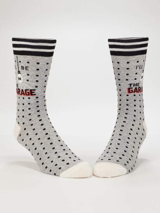 Blue Q's I'll Be In The Garage M-Crew Socks feature gray fabric with black polka dots, white toes and heels, black and white striped cuffs, plus "I’LL BE IN THE GARAGE" in black and red—perfect garage gifts for him.