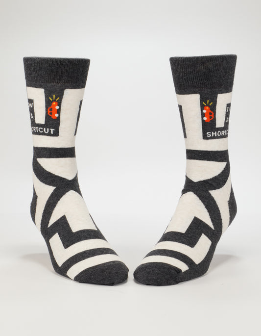 Blue Q’s I Know A Shortcut M-Crew Socks feature black and white maze patterns, a small red ladybug, and "NEW SHORTCUT" text near the top. Made of cotton and available in men’s size 7-12.