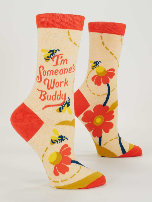 The Blue Q "I'm Someone's Work Buddy Crew Socks" are beige with red toes, heels, and cuffs. They feature bees, yellow and red flowers, swirly lines, and "I'm Someone's Work Buddy". Soft combed cotton fits women's shoe size 5-10.