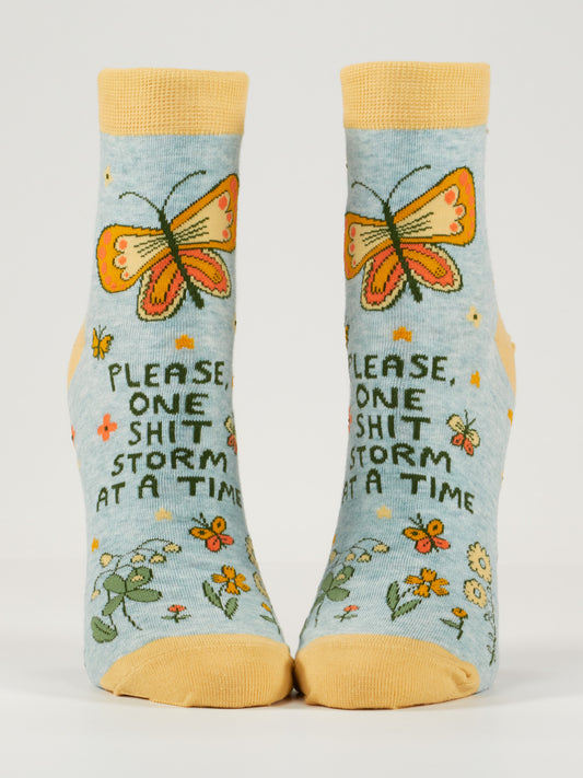 Blue Q’s “Please, One Shitstorm At A Time” W-Ankle Socks are blue combed cotton with yellow toes, heels, cuffs, an orange butterfly, flowers, and the phrase printed on the front.