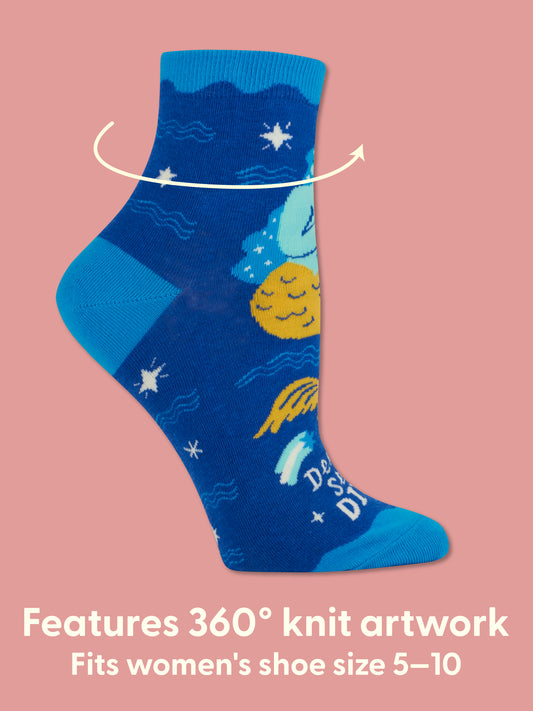 The Deep Sea Diva W-Ankle Socks by Blue Q, made of blue combed cotton with vibrant knit moon, sun, clouds, and stars art, appear on a pink background. White text: 360° knit artwork. Fits women’s shoe size 5-10. Perfect for pop music sock fans!.