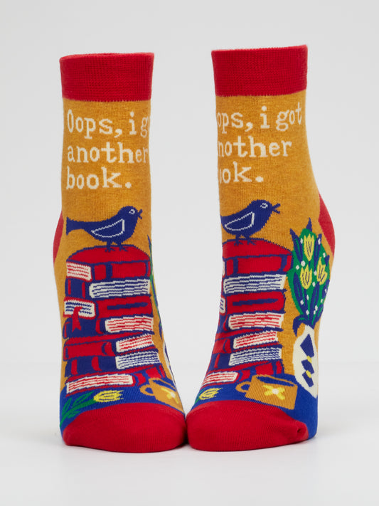 Add a literary touch to your wardrobe with Blue Q’s “Oops, I Got Another Book. W-Ankle Socks.” These vibrant women’s ankle socks feature whimsical stacks of books, cheerful birds, and a plant alongside the playful phrase “Oops, I got another book.” Primarily in red, yellow, and blue hues, they’re the perfect gift for any reading enthusiast.