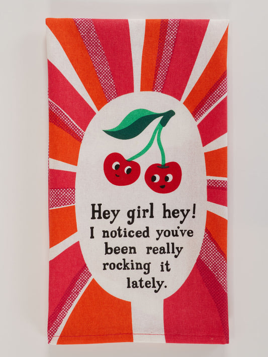 The Blue Q "Hey Girl Hey! I Noticed You've Been Really Rocking It Lately." dish towel features two cartoon cherries with faces and green leaves, surrounded by red and orange rays, plus the uplifting message: “Hey girl hey! I noticed you’ve been really rocking it lately.”.