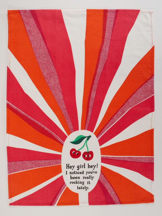 The Blue Q "Hey Girl Hey! I Noticed You’ve Been Really Rocking It Lately." Dish Towel features red and orange sunburst rays, two smiling cherries, and playful text—perfect for adding cheer to any kitchen.