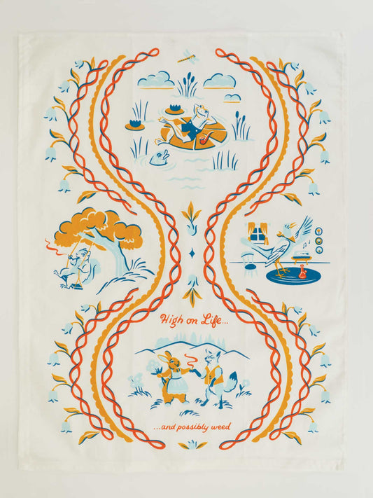 The Blue Q "High On Life...And Possibly Weed Dish Towel" features orange and yellow vines framing scenes of people enjoying nature, cooking, and dancing. "High on Life...and whatever floats your boat or gets you high" appears in red script near the bottom.