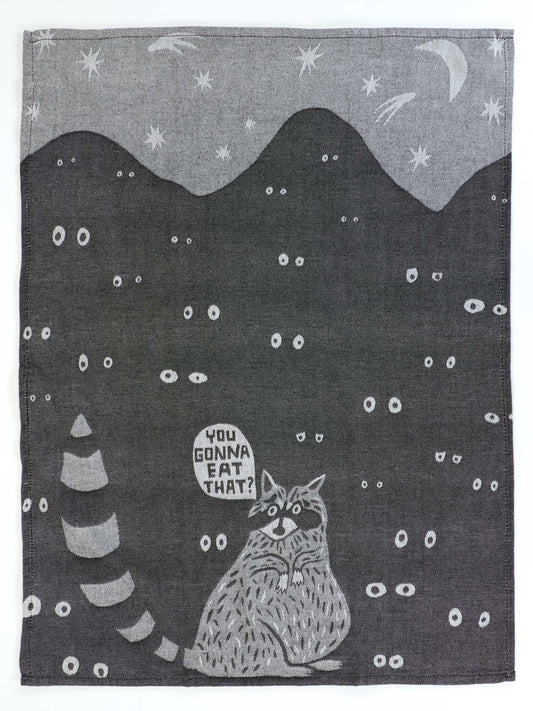 The Blue Q "You Gonna Eat That Dish Towel" features a raccoon with food and glowing eyes, saying "You gonna eat that? Asking for a friend," with mountains, stars, and comets in the background.