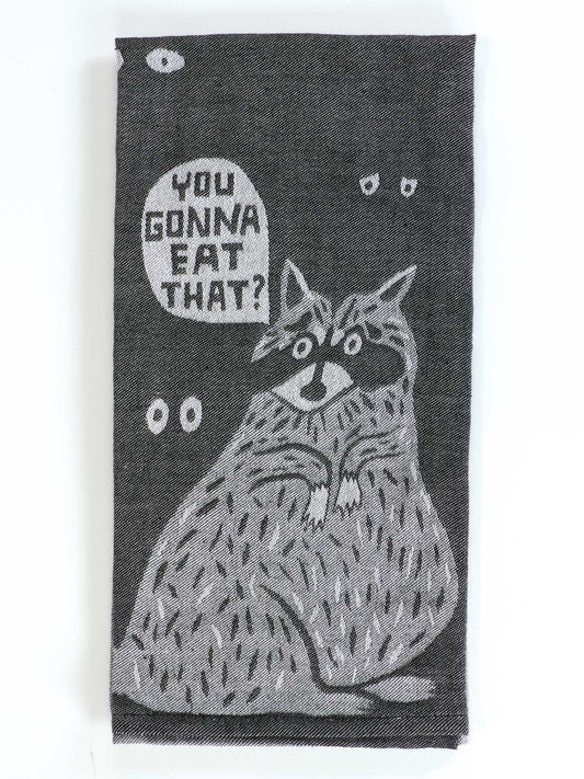 The Blue Q "You Gonna Eat That Dish Towel" is a black and white towel with a cartoon raccoon, wide-eyed and surrounded by smaller eyes, plus a speech bubble asking, "YOU GONNA EAT THAT?—just asking for a friend.