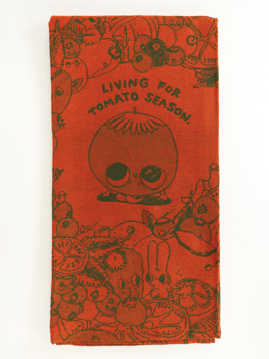 The Living For Tomato Season Dish Towel by Blue Q is a red unbleached cotton towel with a smiling cartoon tomato, the phrase “LIVING FOR TOMATO SEASON,” and doodled veggies like carrots, radishes, and sliced tomatoes.
