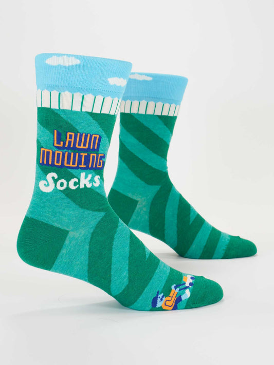 Blue Q’s Lawn Mowing Socks Men's Socks feature a green and blue lawn pattern, white picket fence, clouds, and a mower graphic by the toe. "Lawn Mowing Socks" is printed on the side. Fits most men’s shoe sizes.