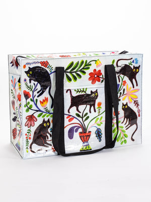 The Here Kitty Shoulder Tote by Blue Q features playful black cat illustrations, vibrant florals, and black handles on a white background—a stylish choice for cat lovers or as a fun alternative to a typical cat carrier.