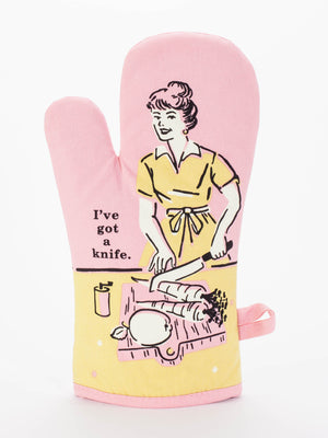 The Blue Q “I've Got A Knife Oven Mitt” features a retro illustration of a woman slicing veggies and the phrase "I've got a knife" on a pink mitt with a light yellow background—perfect for cute kitchen decor or fun accessories.