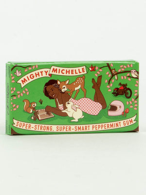 A green box of Blue Q's Mighty Michelle Gum shows an illustrated girl reading with a fawn, rabbit, and squirrel nearby, plus flowers, a motorcycle, and helmet in the background—a fun gift for fans of inspiring historical figures!.