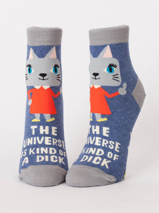 Blue Q’s “The Universe Is A Kind Of A Dick” W-Ankle Socks feature a blue-eyed kitten in a red dress giving a thumbs-up, with the phrase “THE UNIVERSE IS KIND OF A DICK” printed across both cute blue socks.
