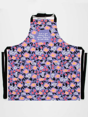 The Blue Q "Just A Girl Staring At A Dinner Asking It To Cook Itself" Apron features colorful floral cotton twill with an adjustable neck strap and extra-long waist ties, perfect for brightening up any kitchen.