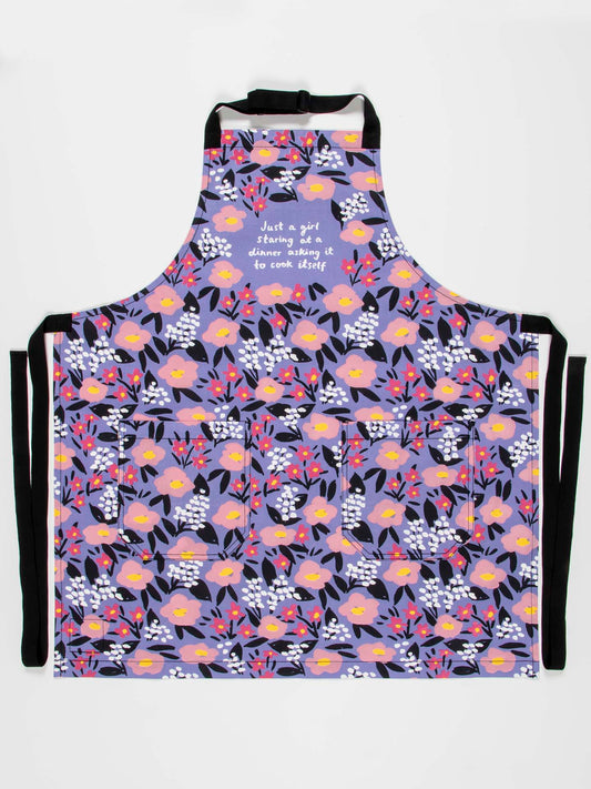 The Blue Q "Just A Girl Staring At A Dinner Asking It To Cook Itself" Apron features colorful floral cotton twill with an adjustable neck strap and extra-long waist ties, perfect for brightening up any kitchen.