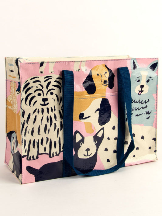 The Happy Dogs Shoulder Tote by Blue Q features dark blue handles and a playful print of illustrated dogs in various breeds and colors on a light pink background—perfect for any dog lover.