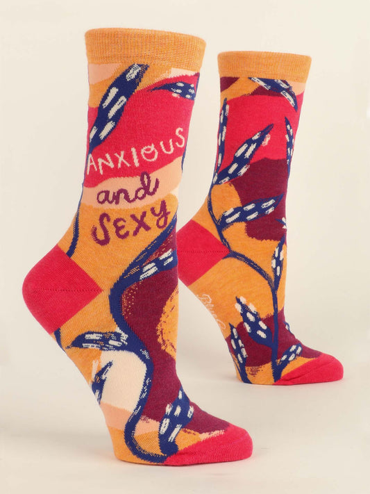 Blue Q’s Anxious and Sexy W-Crew Socks feature a bold, abstract design in orange, pink, red, and purple with blue floral accents. One sock displays "Anxious" and "Sexy" in playful lettering for a vibrant statement look.