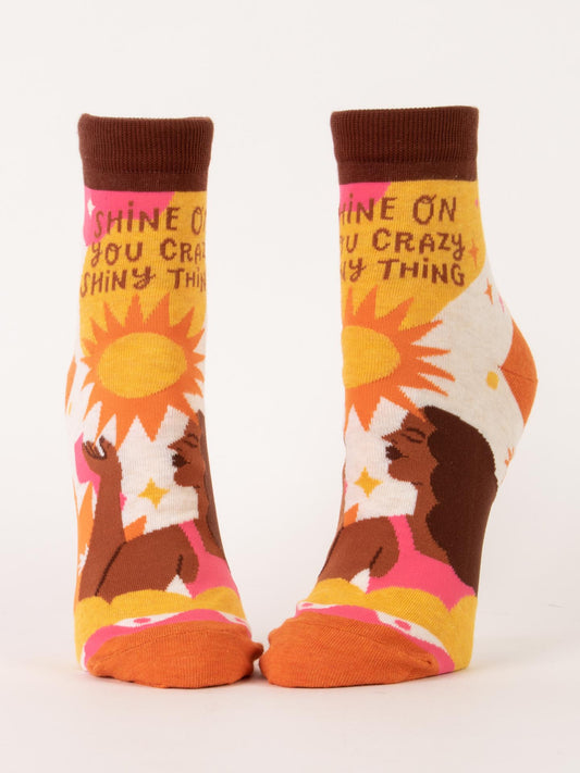 Blue Q's "Shine On You Crazy Shiny Thing" W-Ankle Socks feature a woman with dark hair basking in sunlight among flowers, crafted from a nylon-cotton blend and boldly printed with “Shine on you crazy shiny thing” across the tops.