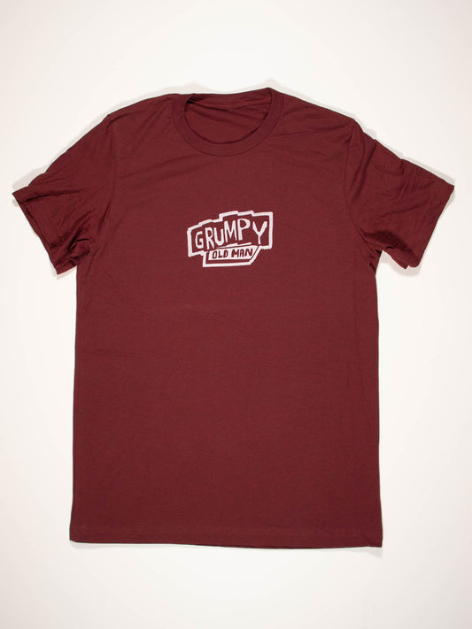 The Blue Q Grumpy Old Man T-Shirt features a maroon color with a bold, vintage white "GRUMPY OLD MAN" graphic on soft Airlume combed cotton and comes in a full range of unisex sizes.