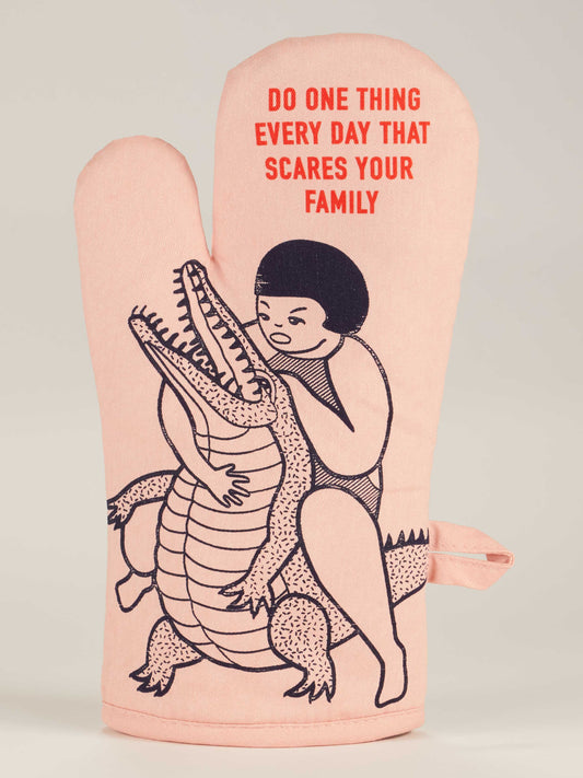 The Blue Q "Do One Thing Every Day That Scares Your Family" Oven Mitt is pink and shows a person wrestling an alligator, with the sayings printed in red at the top—perfect for adding playful mischief to your kitchen.