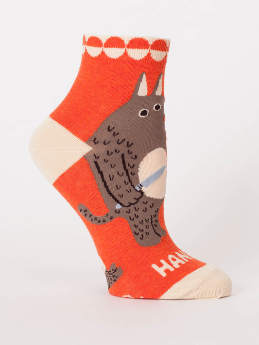The Hangry W-Ankle Socks by Blue Q are bright orange ankle socks made from soft combed cotton, featuring a whimsical brown creature with a blue-striped object. Cream heel and toe with “HAN” on the toe add playful details to these fun socks.