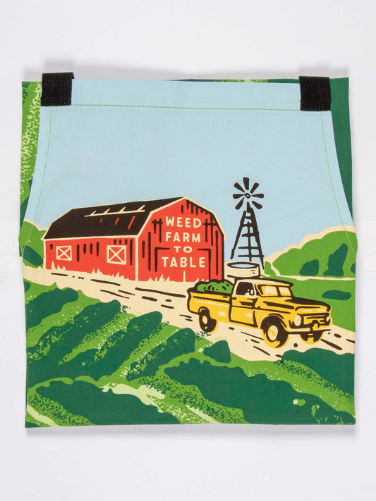 A red barn labeled Weed Farm To Table sits by a windmill, as a yellow truck drives through green fields under blue skies—featured on Blue Q's cotton twill Weed Farm To Table Apron with adjustable neck strap.