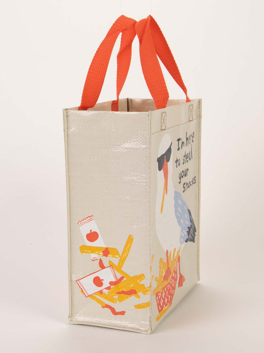 The Blue Q "I'm Here To Steal Your Snacks Handy Tote" is a white reusable bag with red handles, featuring a seagull in sunglasses and playful text—ideal for carrying snacks and beach essentials.