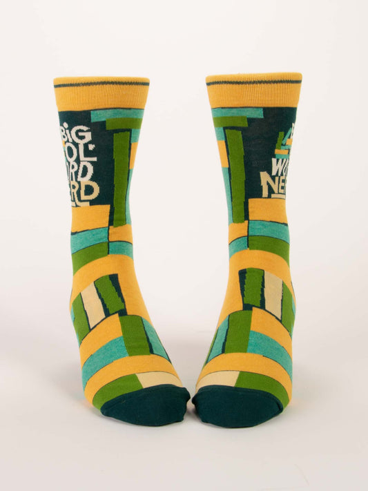 Blue Q Big Ol' Word Nerd M-Crew Socks feature bold geometric yellow, green, and blue patterns. The left sock displays "BIG WOOL NERD" in white text; the right sock shows the phrase partially.