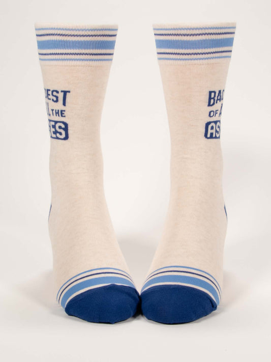 Blue Q’s Baddest Of All The Asses M-Crew Socks are cream-colored combed cotton blend socks with blue toes, heels, striped cuffs, and “BADEST OF ALL THE ASSES” text split between both socks.