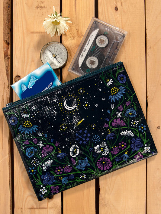 A flat lay of the Blue Q Starry Garden Zipper Pouch, cassette tape, silver compass, blue tissue pack, and a white daisy on wood—evoking the dreamy vibe of night-blooming flowers.