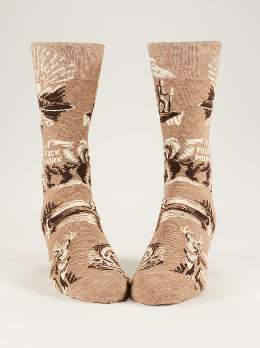 The Blue Q Fuck Work M-Crew Socks are tan novelty socks with western-themed designs like horses, cacti, and lassoing figures. "FUCK WORK" is woven into the cotton blend fabric. They’re displayed standing upright against a plain background.