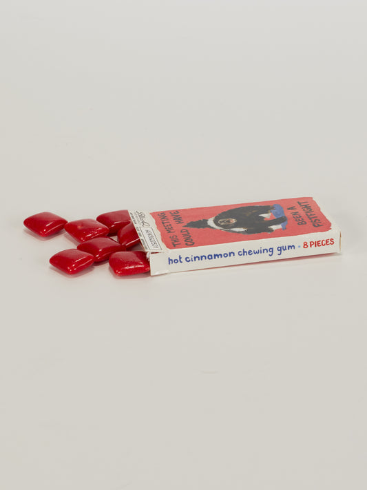 An open Blue Q "This Meeting Could Have Been A Fistfight Gum" box reveals eight red, square cinnamon pieces spilling out. The mostly white box has a red bear graphic. Enjoy the bold flavor—8 pieces in every pack.